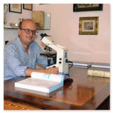 Foto Storica del Professor Alfonso Baldi seduto alla scrivania del suo studio davanti ad un microscopio professionale
